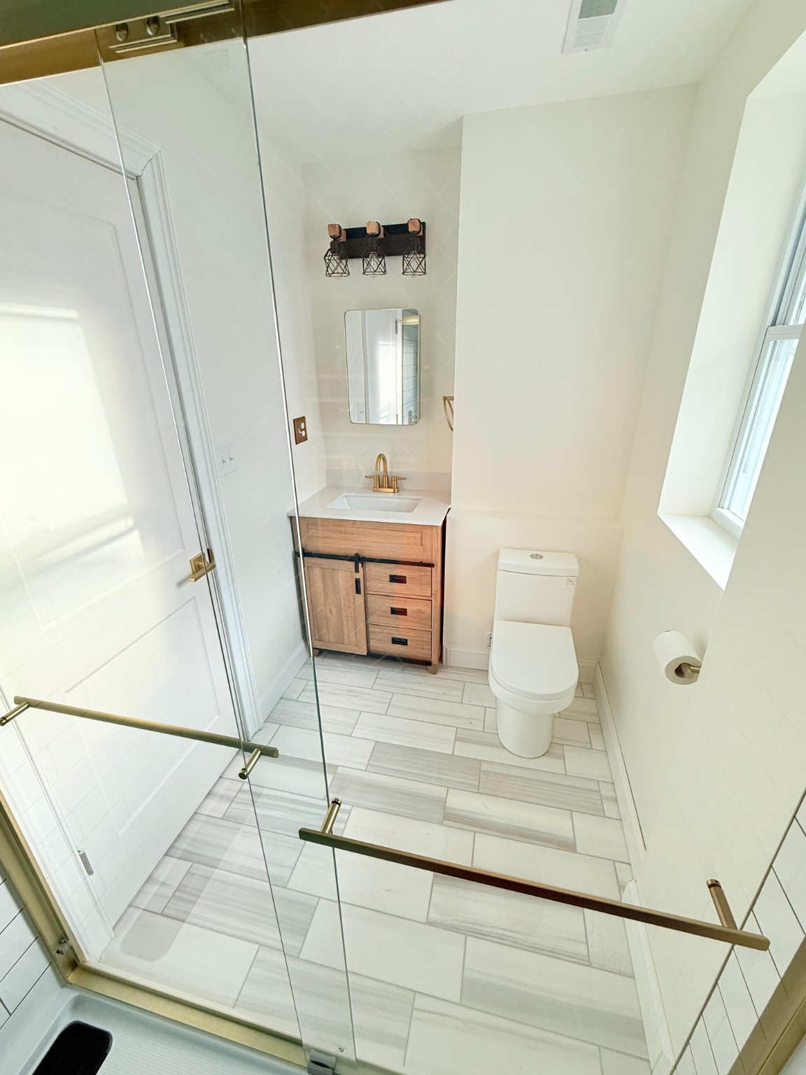 Bright bathroom remodel with glass shower, vanity, tile floor, and toilet