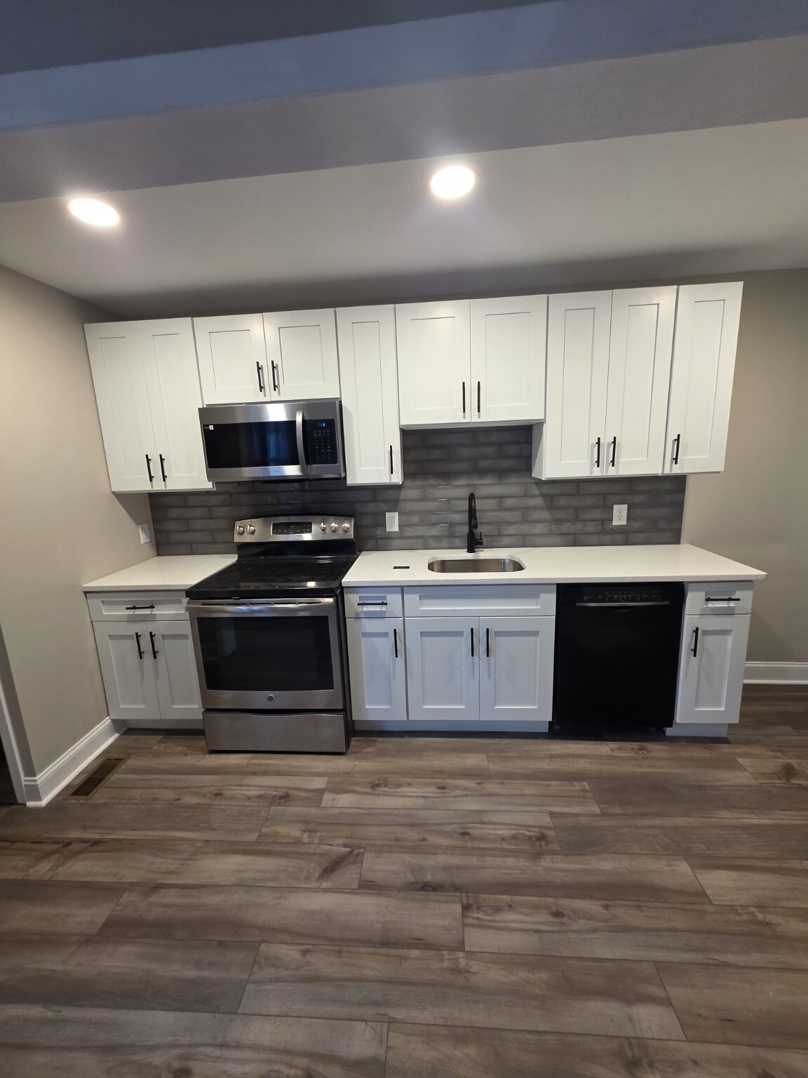Compact kitchen remodel with white cabinets, dark countertops, and plank flooring